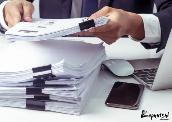 Business Plan Basics: Botswana Template & Guide 9 Man holding well-organized documents at a clean workspace with MacBook and iPhone, emphasizing orderly business planning